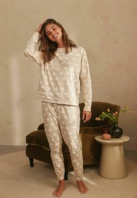Beige pyjama set met een pompoenpatroon, gemaakt van zachte stof. De top heeft een ronde hals, en de broek heeft een getailleerde pasvorm met elastische boorden.