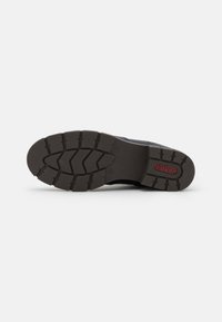 Semelle de chaussure en caoutchouc noir avec des reliefs profonds. Présente une finition texturée et des détails de logo rouges. Conception plate pour une adhérence et une traction stables.