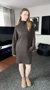 Hnědé pletené šaty s rolákem, dlouhými rukávy a žebrovaným lemem. Doplněné béžovými kotníkovými botami na platformě, vystavené v moderním interiéru.