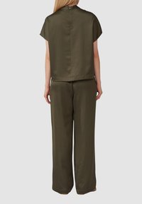Ensemble de pantalons vert olive comprenant un haut à col montant et manches courtes, associé à un pantalon large, fabriqués dans un tissu lisse avec une coupe décontractée.