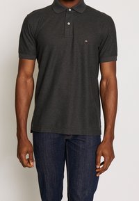 Polo shirt court gris foncé à manches courtes en coton, doté d'une patte de boutonnage à deux boutons et d'un petit logo sur la poitrine gauche. Design ajusté.