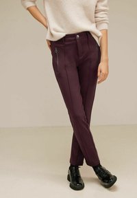 Burgundy-färga skräddarsydda byxor med dragkedjefickor, slät tyg och en välsydd design, tillsammans med svarta snörskor.