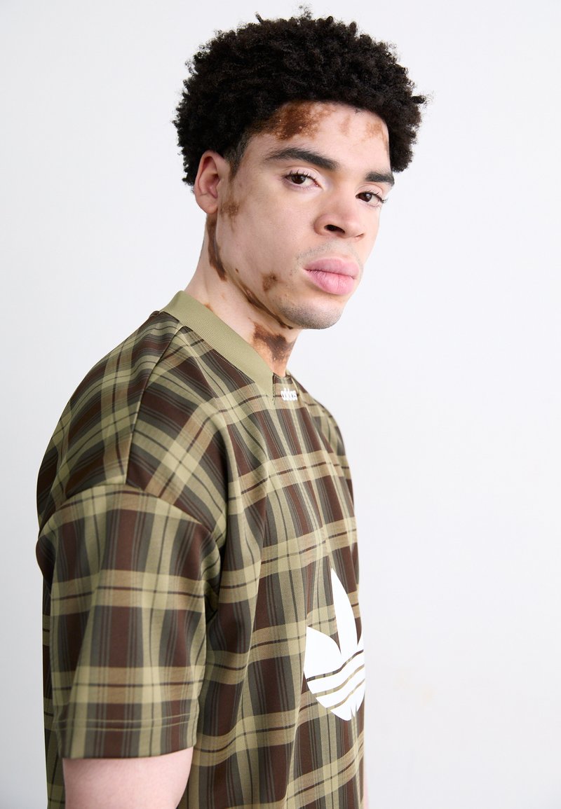 Brązowa i oliwkowa krótkozasięgowa koszula w kratę z białym logo na piersi. Gładka tekstura, okrągły dekolt i casualowy design.