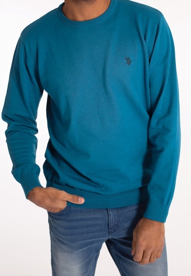 Turkusowy sweter z okrągłym dekoltem, wykonany z gładkiej dzianiny, z żebrowanymi mankietami i dołem. Na piersi znajduje się małe czarne logo.