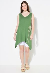 Groene mouwloze tuniek met een V-hals en asymmetrische zoom, met een palmboomgrafiek aan de zijkant. Zacht, lichtgewicht stof.