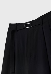 Pantalon noir plissé en tissu lisse, doté d'une ceinture avec une boucle métallique argentée et de poches latérales, présentant une coupe ajustée.