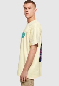 Camiseta de algodón amarilla con un gráfico circular turquesa en el frente y un diseño multicolor en la parte posterior, con mangas cortas y un corte relajado.