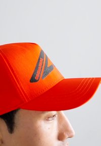 Ljusa orangebasebollkeps med en böjd skärm, med en svart logotypdetalj på framsidan och textil med struktur för en sportig look.