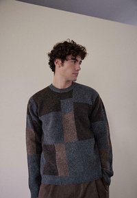 Mehrfarbiger, strukturierter Pullover mit verschiedenen Grautönen, Brauntönen und Blautönen in einem Patchwork-Design; runder Ausschnitt und lange Ärmel.
