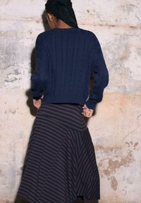 Granatowy sweter dziany z wzorem warkocza, zestawiony z brązowo-granatową spódnicą w paski. Materiał wydaje się miękki, o teksturowanym wykończeniu.