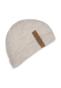 Beżowa, włóczkowa czapka z miękkiej przędzy, z fakturowanym korpusem i ściągaczem. Zawiera brązową etykietę z tekstem.