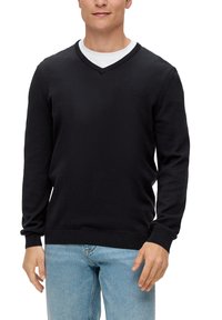 Czarny sweter w serek z gładkiego materiału, z prążkowanymi mankietami i dołem, noszony na białym T-shircie z okrągłym dekoltem, w zestawie z jasnoniebieskimi dżinsami.