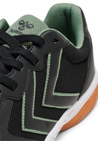 Černá sportovní bota s vrškem z prodyšné síťoviny a gumovou podešví. Zelené akcenty a prošívání zvýrazňují design. Má kulaté tkaničky a polstrovaný jazyk.