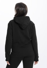 Melns kapuces krekls, izgatavots no mīkstas auduma. Aprīkots ar kangaroo kabatu un ribinātiem piedurknēm. Dizains ir brīva piegriezuma ar noapaļotu apakšmalu.