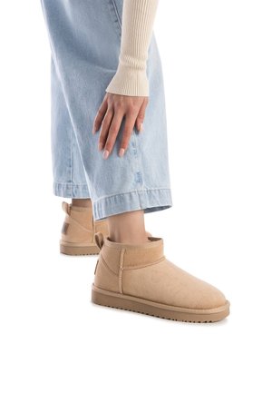 Botas de tobillo de ante beige con punta redondeada, adornos cosidos y suela de goma, combinadas con jeans de pierna ancha de color azul claro.