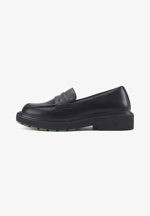 Black leather loafers featuring a stitched, raised strap, chunky sole, and green accent on the tread. Classic, rounded toe shape.