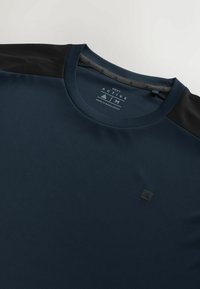 Marineblå aktiv t-shirt med sorte skulderdetaljer, rund halsudskæring, glat tekstur og et logomærke foran. Fremstillet af fugttransporterende stof.