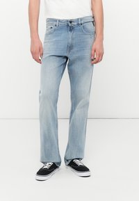 Blugi din denim de culoare bleu deschis, cu un design drept, ușor decolorate, cinci buzunare și bucle pentru curea; asortați cu adidași negri.