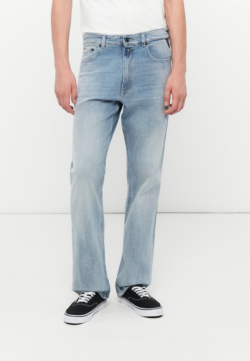 Blugi din denim de culoare bleu deschis, cu un design drept, ușor decolorate, cinci buzunare și bucle pentru curea; asortați cu adidași negri.