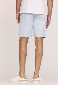 Shorts en coton bleu clair avec des revers, associés à des baskets blanches avec des accents beiges. Texture lisse et design décontracté.