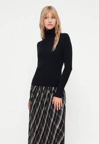 Jersey de cuello alto negro con mangas largas, diseño ajustado, hecho de un material suave, combinado con una falda maxi texturizada y estampada.
