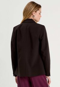 Blazer noir ajusté avec fermeture à un bouton, épaules structurées et finition lisse. Présente des manches longues et un dos droit.