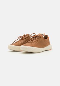 Des baskets brunes en cuir texturé, dotées d'un panneau latéral en maille, d'une semelle en caoutchouc blanc avec un design à motifs et d'un accent orange au niveau du talon.