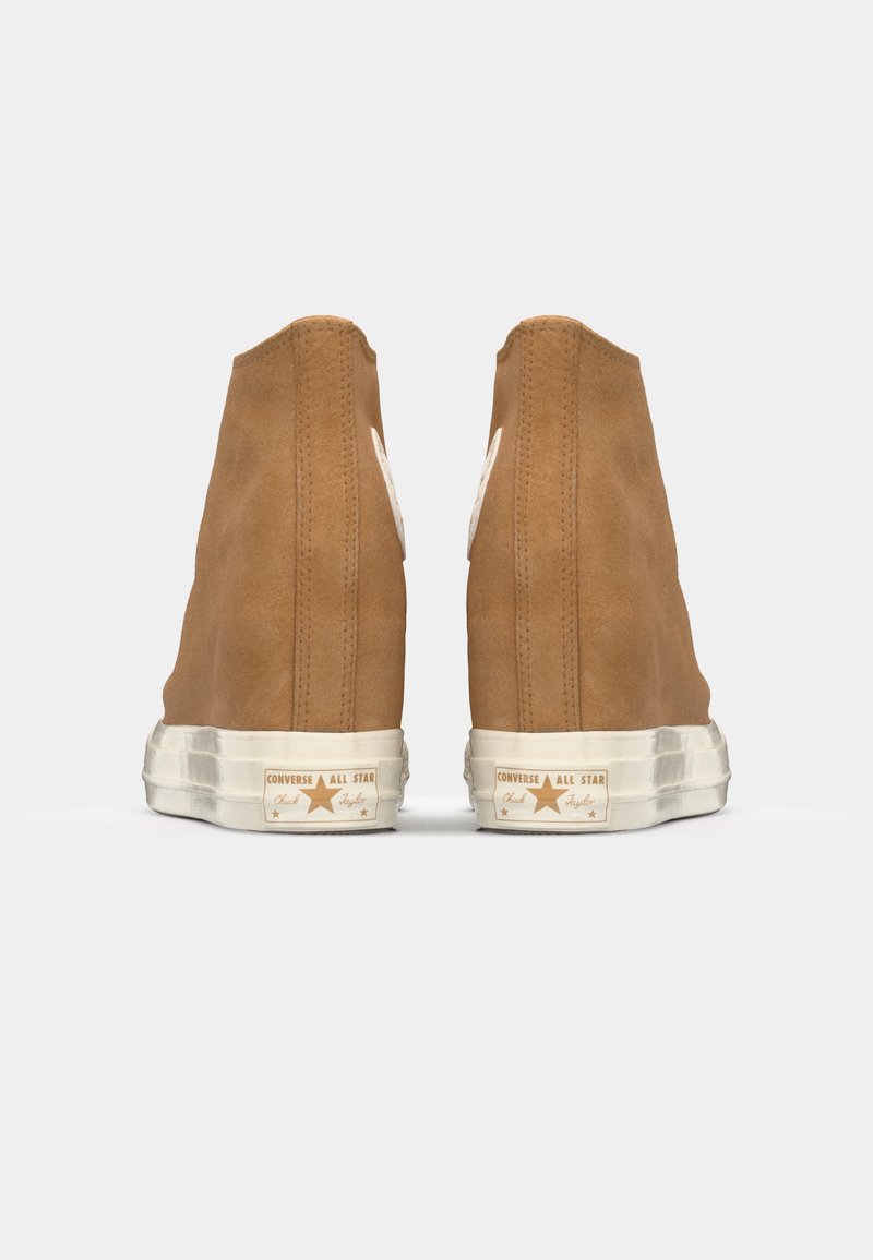 Sneaker alte in suede marrone con un logo bianco sul tallone e una suola in gomma texture. Branding distintivo sui lati e sul retro.