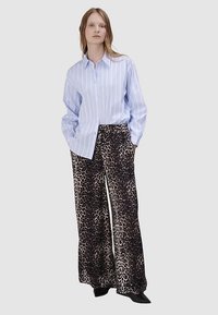 Jasnoniebieska koszula w paski z guzikami, zestawiona z szerokimi spodniami w panterkę o luźnym kroju i gładkiej tkaninie. Czarne obuwie.