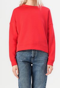 Sweatshirt rouge avec un col rond et des épaules tombantes. Présente un design court, des poignets côtelés et une texture de tissu douce et lisse.