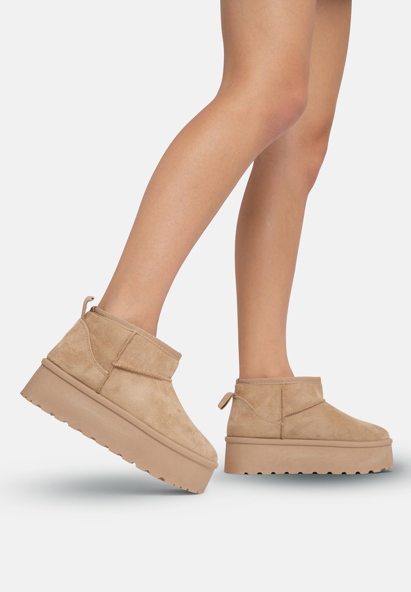 Botas de tobillo beige de ante, con una suela de plataforma, punta redonda y lengüeta en la parte posterior. El diseño es sencillo y con líneas limpias.