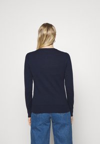 Tmavě modrý svetr s dlouhým rukávem a kulatým výstřihem, vyrobený z měkkého pleteného materiálu. Pružný střih s žebrovanými manžetami a lemem.