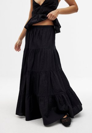 Gonna maxi nera a strati con tessuto testurizzato, una vita alta e una silhouette svasata. Indossata con scarpe con dettagli in pizzo.