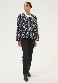 Floral quilted jacket in dark blue with white flowers, featuring a round neck, open front, and two patch pockets. Paired with black jeans.