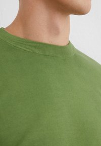 Zielona bawełniana koszulka z okrągłym dekoltem, z prążkowanym kołnierzykiem, gładką fakturą, dopasowanym krojem i minimalnym zdobieniem, podkreślająca swoją prostą formę.