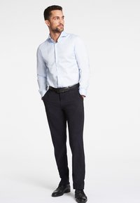 Camicia azzurro chiaro con maniche lunghe e colletto, abbinata a pantaloni blu scuro e scarpe nere, dotata di cintura e vestibilità slim.
