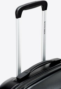 Mango extensible de equipaje plateado con agarre negro, sujeto a una maleta negra, con la marca "WITTCHEN" visible en el lateral.