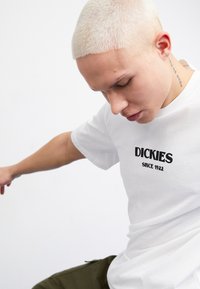 Camiseta de algod�ón blanco con el logotipo negro de "DICKIES" y el texto "DESDE 1922". Mangas cortas, corte standard, diseño minimalista, textura suave.