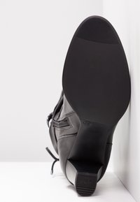 Botte en cuir noir avec un bout rond, semelle en caoutchouc texturée et un talon haut. Dispose d'une fermeture éclair latérale et de détails de couture décoratifs. Taille 38.