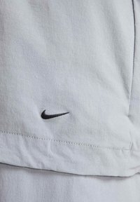 Ropa Nike de color gris claro con una tela texturizada, que presenta un pequeño logo negro bordado cerca del dobladillo y un detalle de costura en contraste.