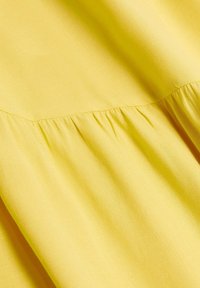 Tissu jaune vif avec des fronces créant des plis doux et de la texture, mettant en évidence une couture qui traverse horizontalement le matériau.