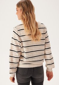 Cremefarbenes Strickpullover mit horizontalen schwarzen Streifen und Lochmustern, mit gerippten Bündchen und Saum. Einfaches, lässiges Design.