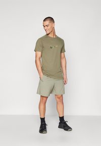 Olive green Nike t-shirt with a textured logo, paired with light green shorts. Model wearing black athletic shoes and socks.