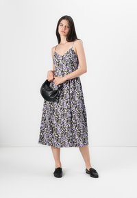 Blumen-Midi-Kleid mit dünnen Trägern in lila, schwarz und weißen Mustern; kombiniert mit einer schwarzen Handtasche und schwarzen Slippern. Glatte Textur.