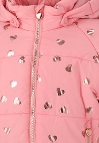 Veste doudoune rose avec des motifs de cœurs métalliques, fermeture éclair sur le devant et capuche. Comprend des accessoires en métal brillant et des tirettes en forme de cœur.