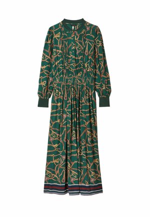 Langes grünes Kleid mit einem goldenen und burgunderfarbenen Kettenmuster, plissiertem Oberteil und gerafftem Bund, kombiniert mit burgunderfarbenen Blockabsatzschuhen.