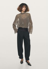 Gennemsigtig, langærmet top med blomsterformede perleudsmykninger i grå, kombineret med sorte højtaljede bukser og spidse flade sko.