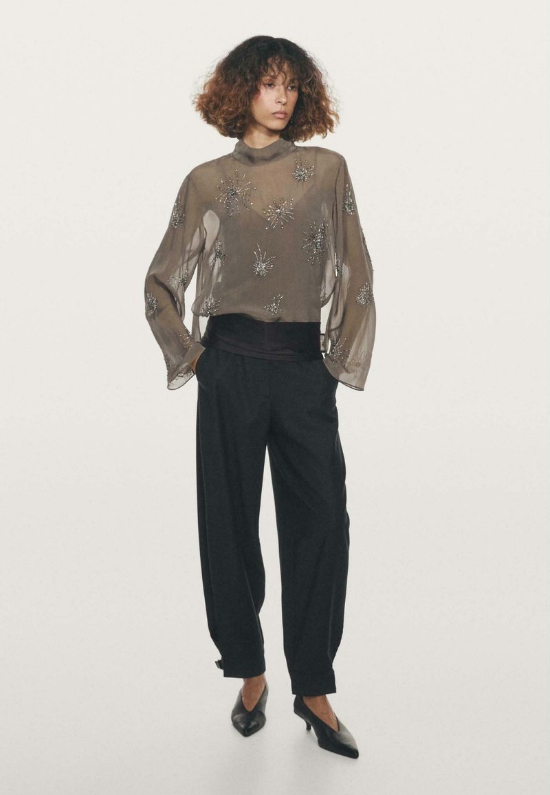 Top trasparente a maniche lunghe con decorazioni floreali in perline grigie, abbinato a pantaloni neri a vita alta e ballerine con punta.