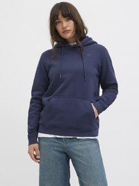 Felpa blu navy realizzata in tessuto morbido, con tasca frontale e coulisse regolabili. Indossata con jeans in denim blu chiaro.