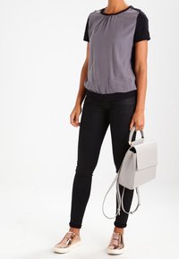 Grå och svart t-shirt med korta ärmar och draget midja, matchad med svarta skinny jeans och en ljusgrå axelväska. Metalliska slip-on skor.